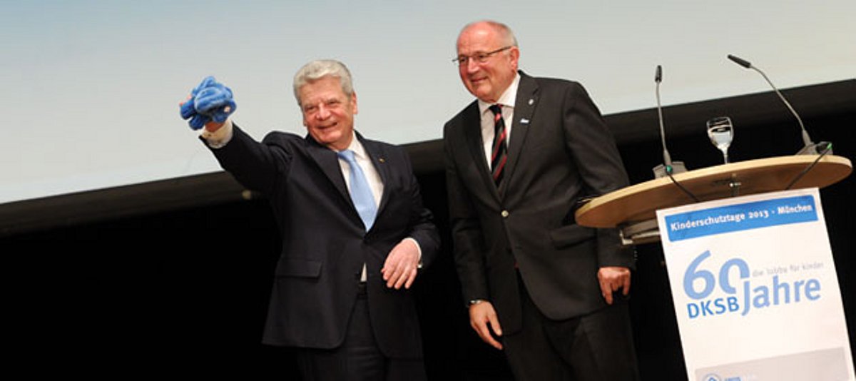 Bundespräsident Joachim Gauck (l) winkt am 03.05.2013 in München bei der Jubiläumsfeier 60 Jahre Kinderschutzbund mit einem blauen Stoffelefanten als der Präsident des DKSB, Heinz Hilgers neben ihm steht.