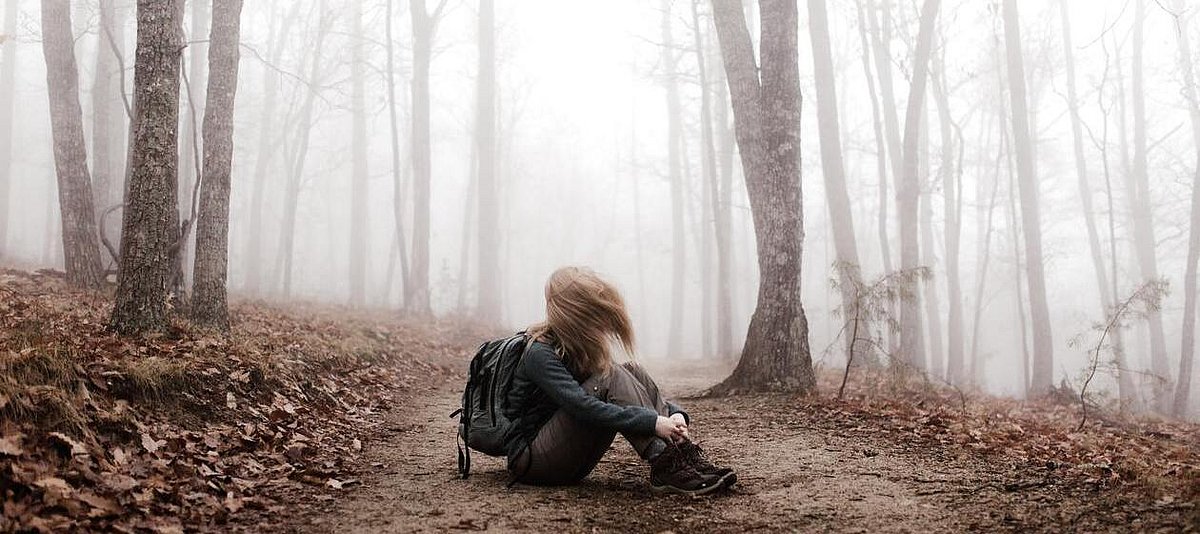 Ein Mädchen sitzt allein im Laub auf einem Waldweg in einem Winterwald.