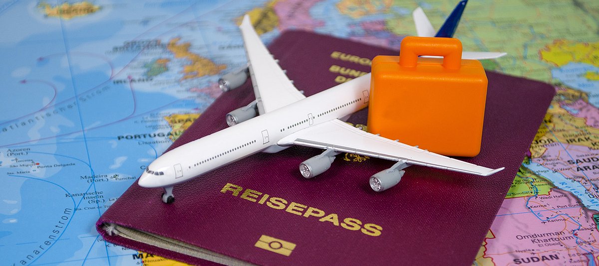 Reisepass mit Miniaturflugzeug und -koffer