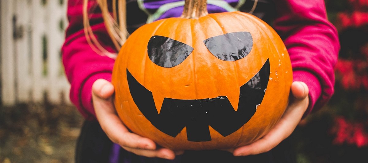 Kind hält einen bemalten Kürbis für Halloween in den Händen