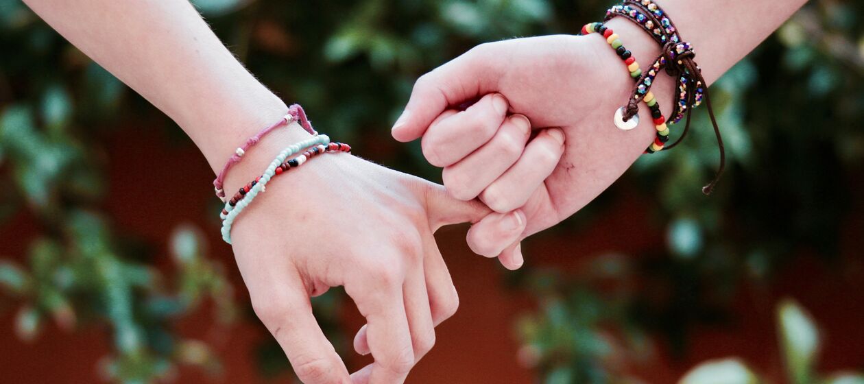 Zwei Jugendliche mit bunten Armbändern halten sich den den Händen