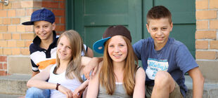 Vier Teenager sitzen glücklich lächelnd auf einer Treppe.