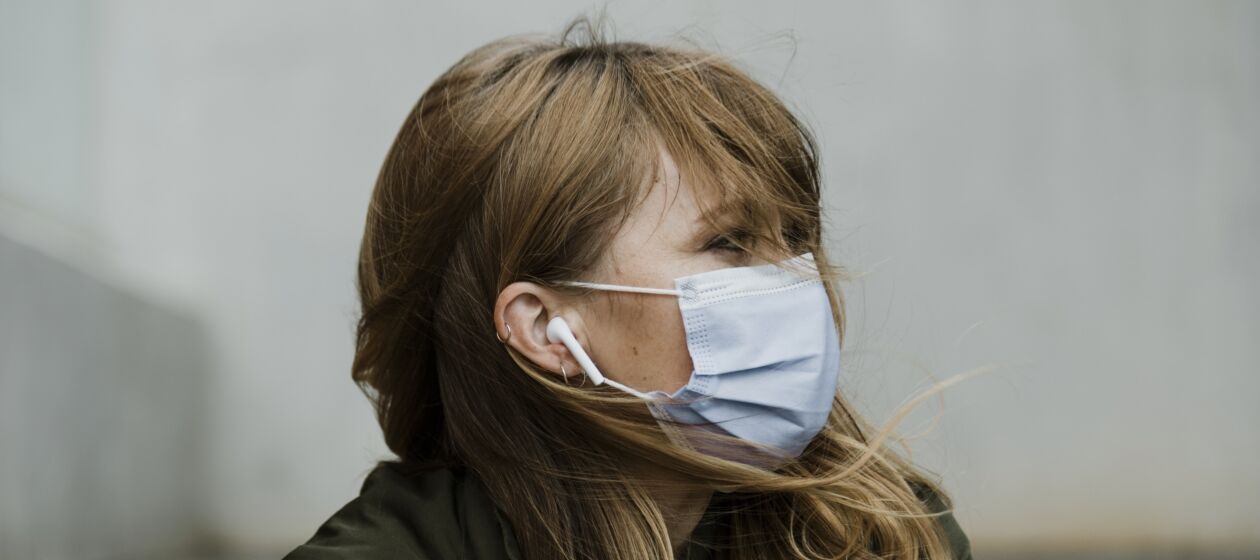 Frau mit Mundschutz und Kopfhörern schaut zur Seite