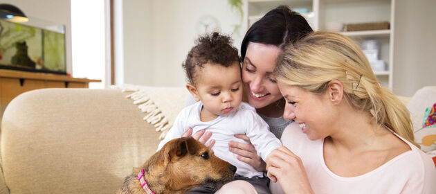 Zwei lesbische Frauen mit Kind und Hund auf dem Sofa.