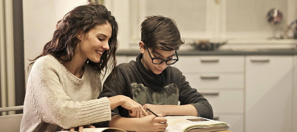 Eine Person hilft einer anderen jüngeren Person beim Lesen und Schreiben.