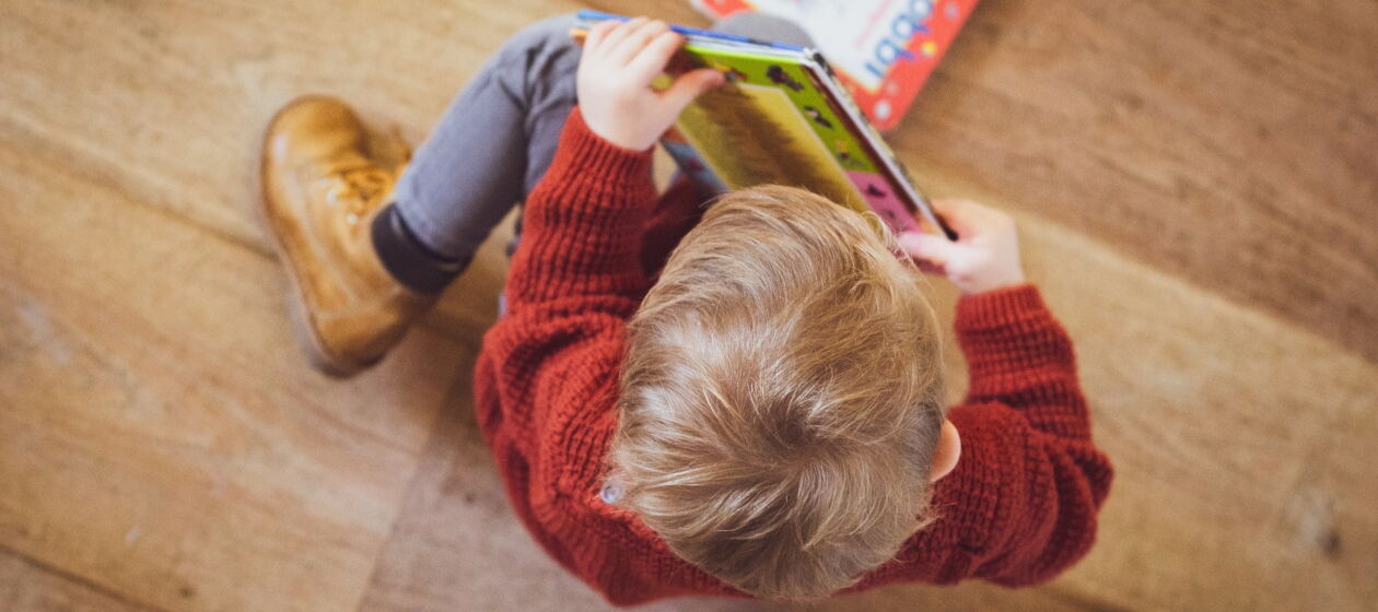 Ein kleines Kind ist von oben zu sehen, in der Hand hält es ein Buch