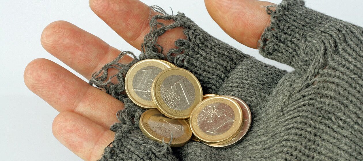 Hände mit abgeschnittenen Handschuhen halten einzelne Geldmünzen