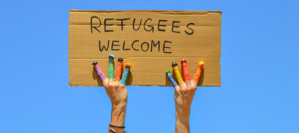Bunte Hände halten ein Schild mit dem Text Refugees welcome hoch