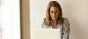 Frau mit Kopfhörern sitzt vor Laptop und scheint digital zu arbeiten