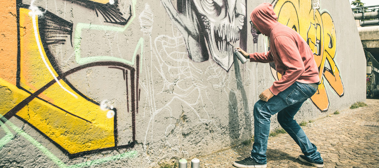 Ein Sprayer gestaltet ein Graffiti auf einer Mauer.