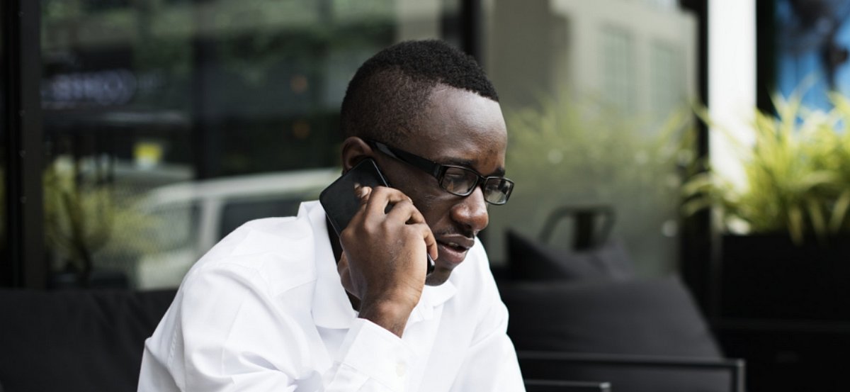 Ein Mann mit dunkler Hautfarbe sitzt an einem Tisch und telefoniert