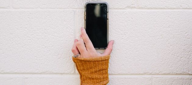 Eine Hand hält ein Smartphone gegen eine Wand