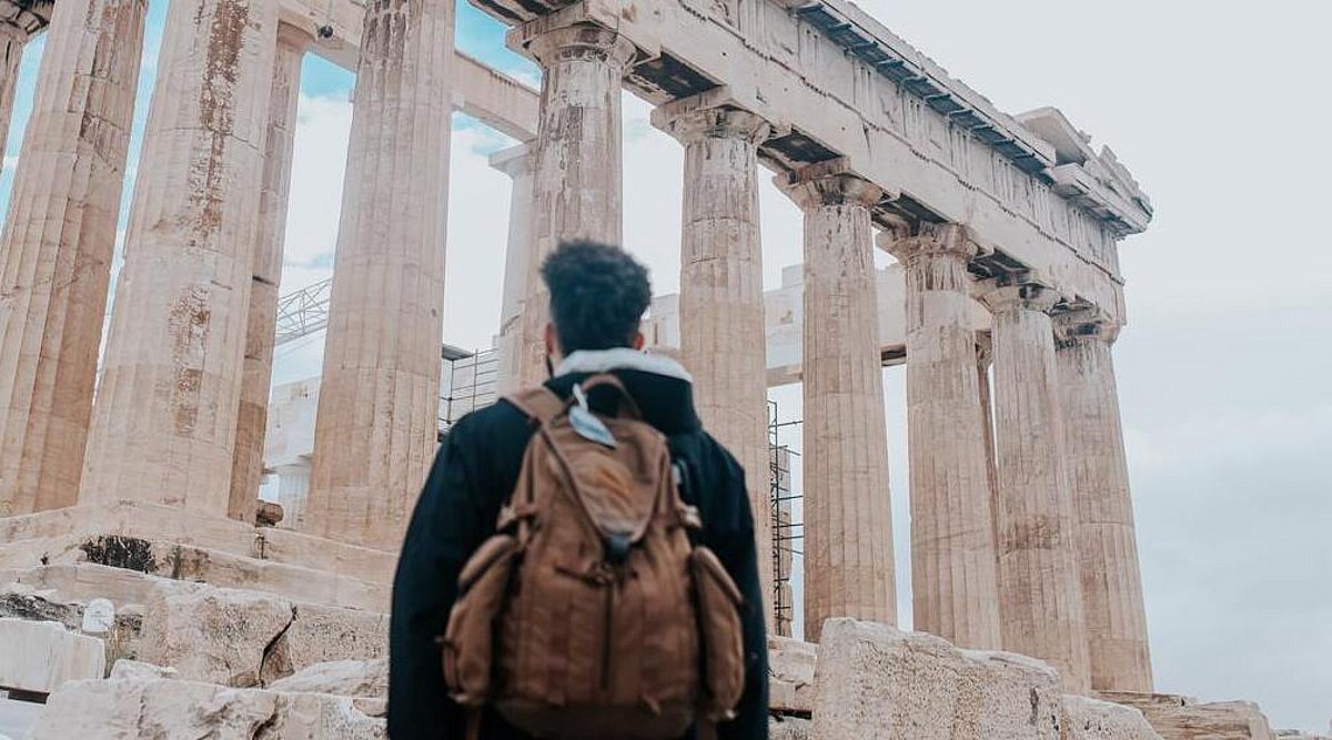 Junger Mann, der einen Rucksack trägt, steht vor der Acropolis in Griechenland und schaut diese an.
