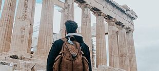 Junger Mann, der einen Rucksack trägt, steht vor der Acropolis in Griechenland und schaut diese an.