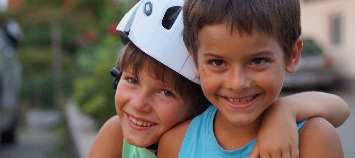 Ein Jugne mit Fahrradhelm umarmt einen anderen Jungen, beide lächeln