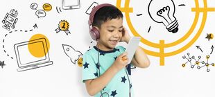 Kleiner Junge mit Smartphone und Kopfhörern vor einer Wand mit Zeichnungen zum technischen Fortschritt