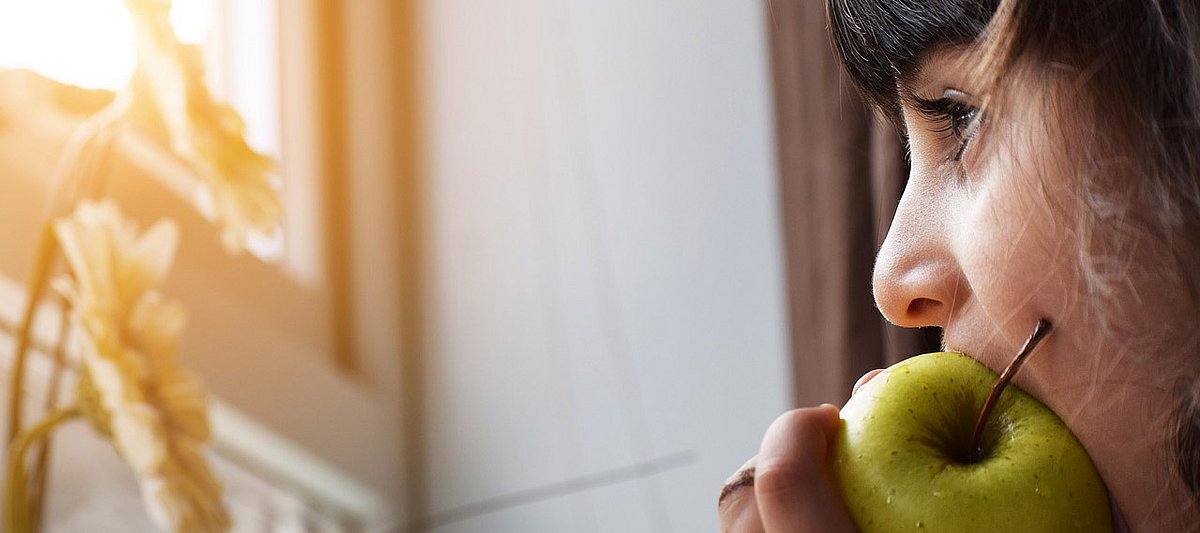 Ein Mädchen beißt in einen Apfel und schaut aus dem Fenster.