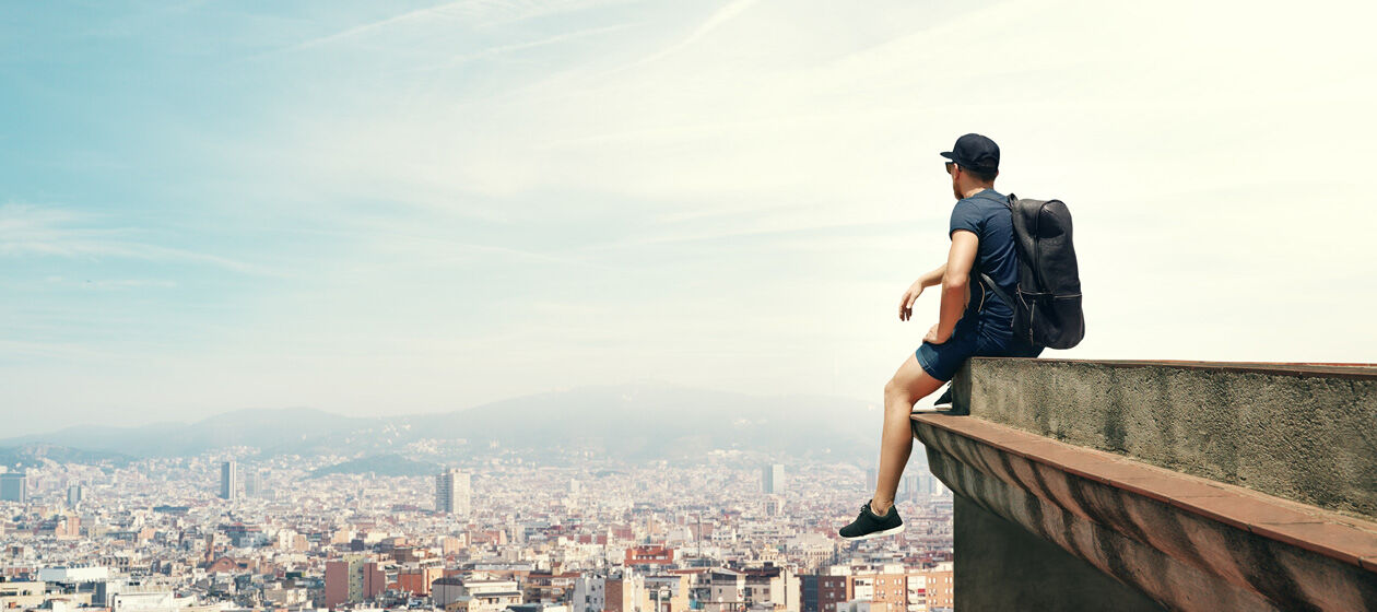 Junger Mann sitzt auf Dach und blickt über Großstadt
