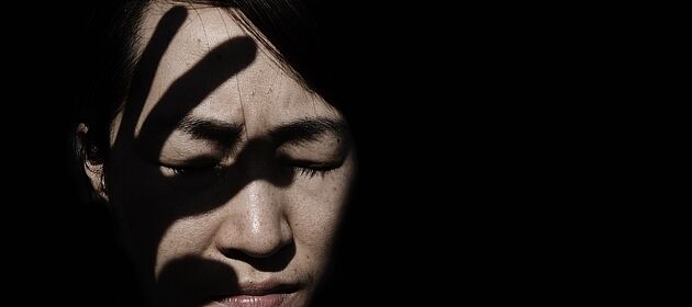 Eine Frau kneift die Augen zu, über ihrem Gesicht liegt der Schatten einer ausholenden Hand