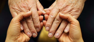 Die Hände eines jungen Erwachsenen halten die Hände eine alten Menschen.