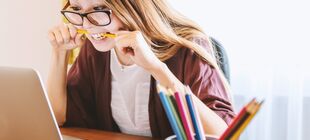Eine Schülerin sitzt vor einem Laptop und beißt auf einen Bleistift