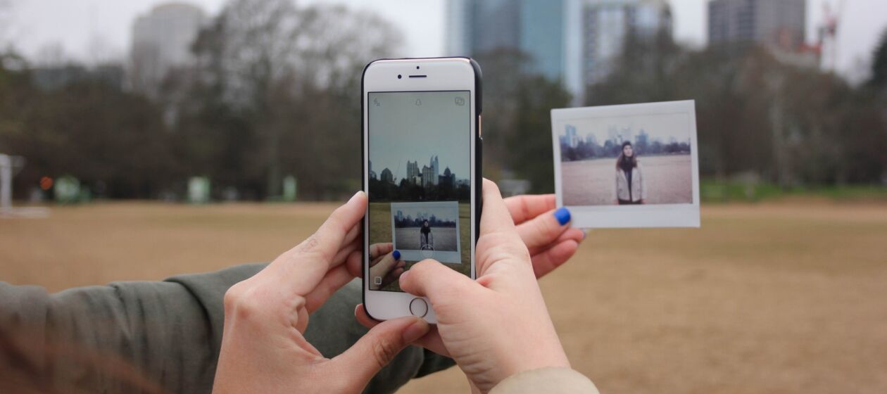 Mit dem Handy wird ein analoges Foto vor einer Stadtskyline abfotografiert