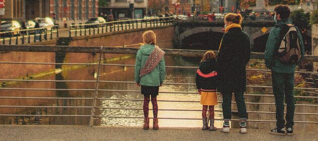 Zwei Erwachsene und zwei Kinder stehen auf einer Brücke, die Erwachsenen tragen eine Mund-Nase-Bedeckung