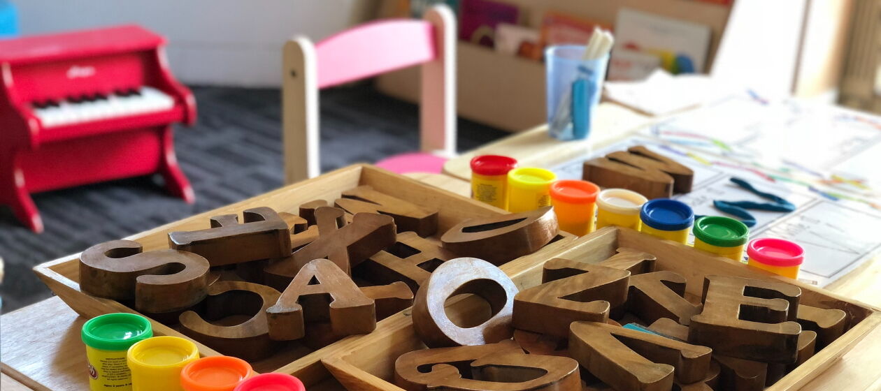 In einem Kita-Raum liegen auf dem Tisch Fingerfarben, Papier und eine Kiste mit einzelnen Buchstaben
