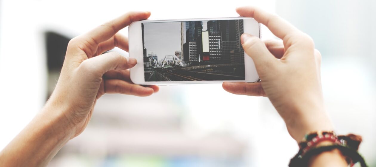 Junger Mensch hält ein Smartphone hoch, auf dem eine Großstadtkulisse zu sehen ist