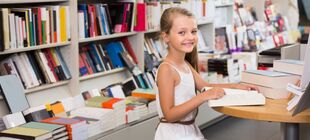 lächelndes Mädchen mit aufgeschlagenem Buch an einem Tisch in Buchhandlung