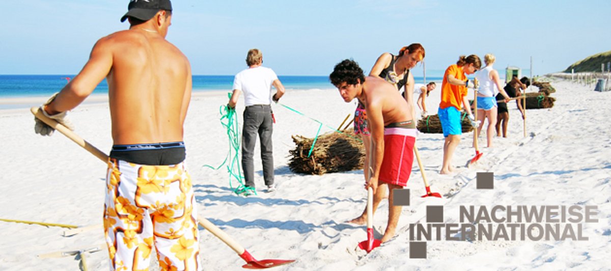 Junge Menschen arbeiten mit Schaufeln an einem Strand 