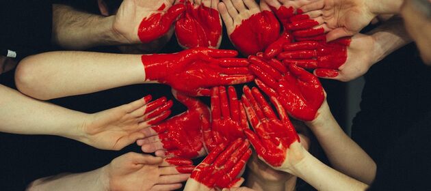 Viele verschiedene Hände sind zum Teil rot angemalt und formen gemeinsam ein Herz