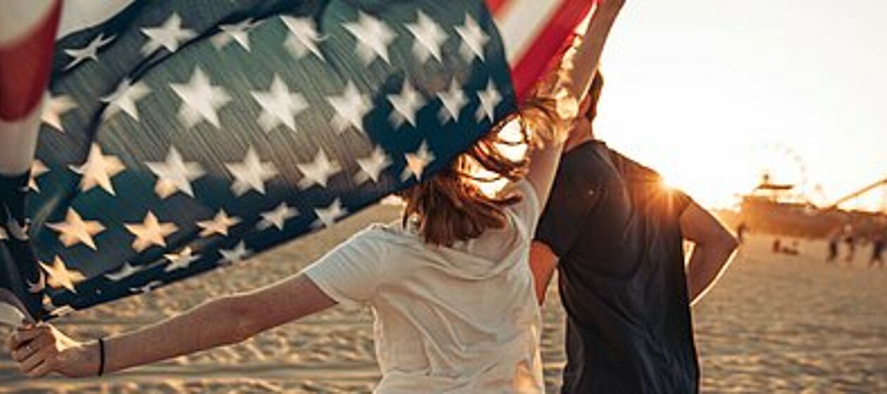 Ein junger Mann und eine junge Frau laufen mit einer US-Flagge über Sand