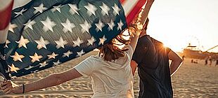 Ein junger Mann und eine junge Frau laufen mit einer US-Flagge über Sand