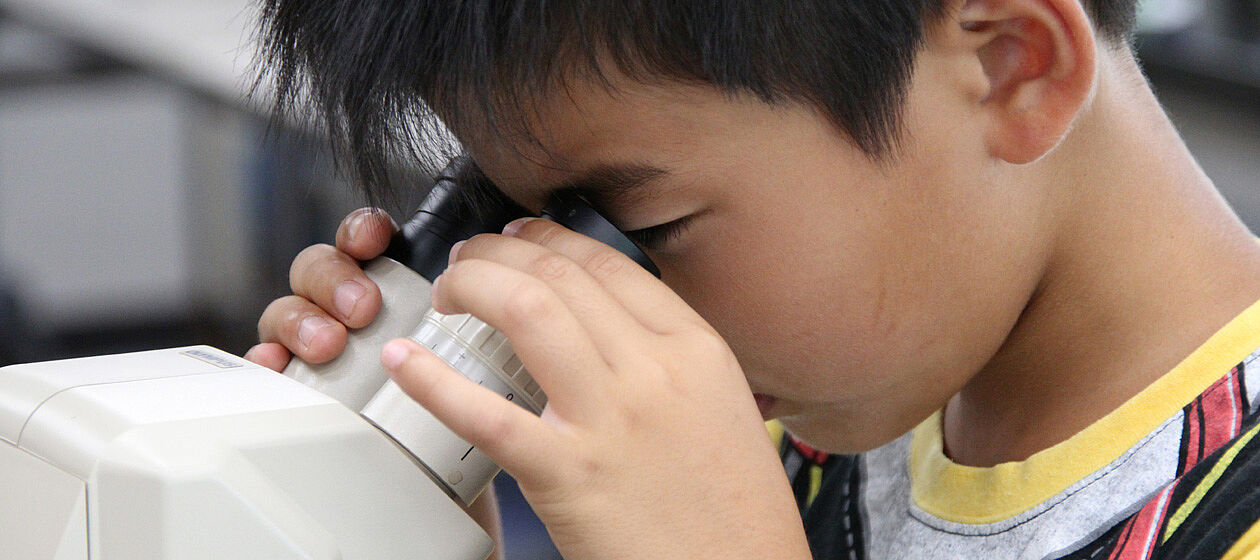 Asiatischer Junge blickt durch Mikroskop 