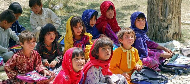Afghanische Schulkinder sitzen mit bunter Kleidung und Schulutensilien auf dem Boden