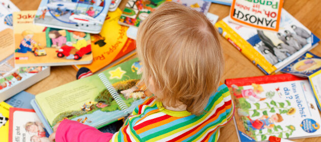 ein Kleinkind sitzt zwischen mehreren Büchern und schaut sich eins an