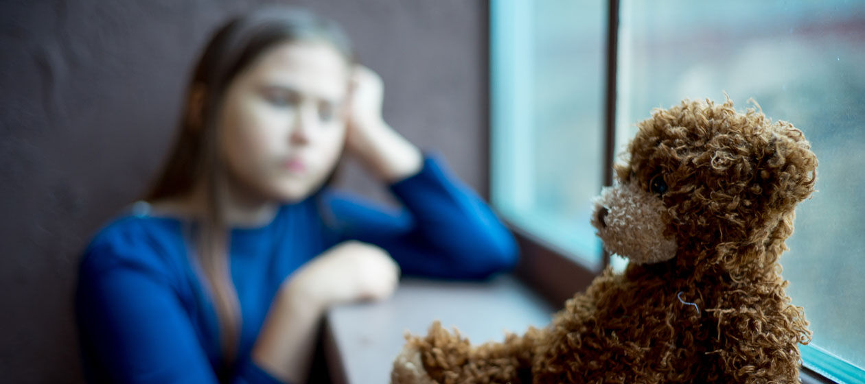 Ein trauriges Mädchen schaut auf ihren Teddy auf der Fensterbank. 