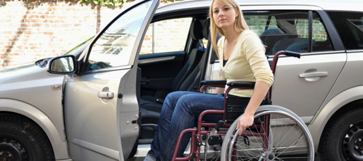 Eine junge Frau im Rollstuhl ist dabei ihr Auto einzusteigen