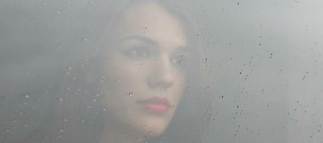Eine Frau blickt traurig durch ein verregnetes Fenster.