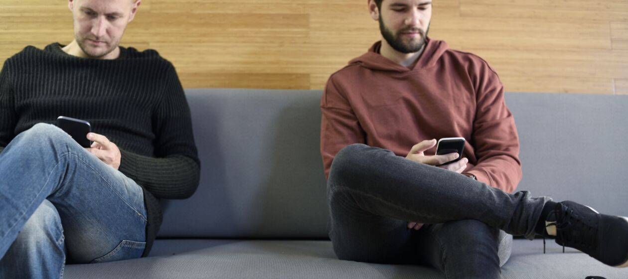 Zwei junge Männer sitzen auf einem Sofa und schauen auf ihre Smartphones