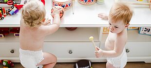 Zwei Kleinkinder stehen vor einem Tisch mit Spielsachen