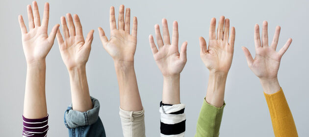 Sechs Hände von Jugendlichen sind nach oben gestreckt, wie bei einer Abstimmung.
