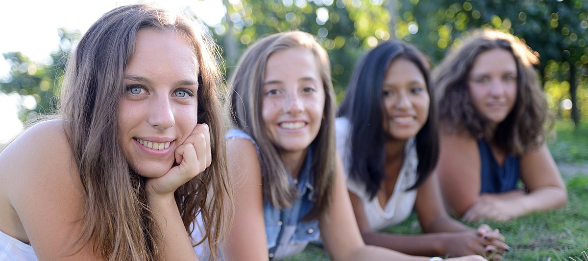 Vier jugendliche Mädchen liegen nebeneinander lächelnd in einer Reihe auf einer Wiese