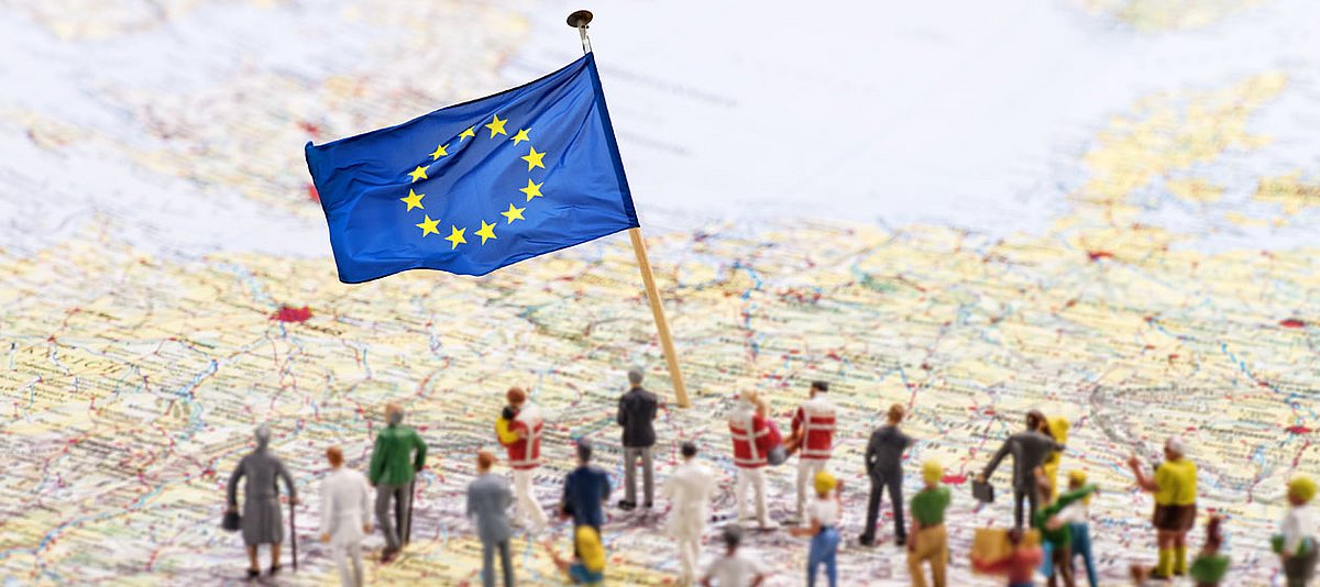 Miniaturfiguren stehen auf einer Landkarte mit einer Europa-Flagge. 