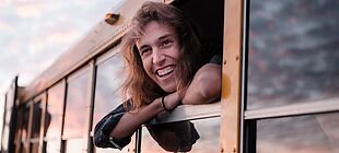 Eine Person schaut lachend aus einem Zugfenster