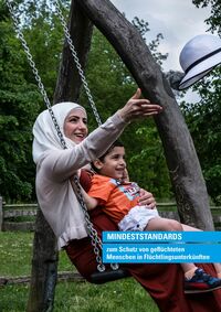 Titel: Mindeststandards zum Schutz von geflüchteten Menschen in Flüchtlingsunterkünften - Beschreibung: Das Bild zeigt eine Frau auf einer Schaukel zusammen mit ihrem etwa dreijährigen Sohn, der auf ihrem Schoss sitzt. Sie trägt ein weißes Kopftuch u