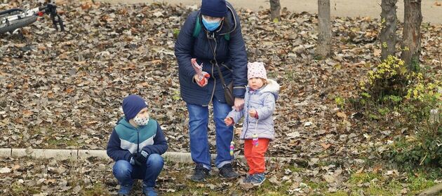 Eine Mutter mit einem Jungen und einem Mädchen am herbstlichen Seeufer. Die Mutter und der Junge tragen einen Mund-Nase-Schutz.