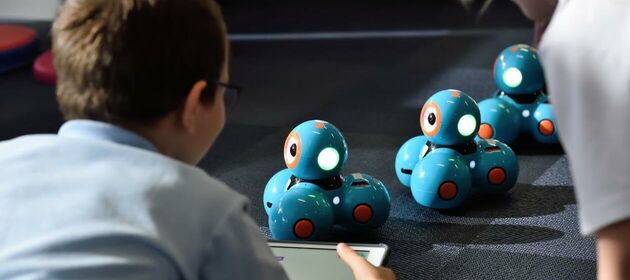 Ein Junge steuert mit einem Tablet drei Roboter