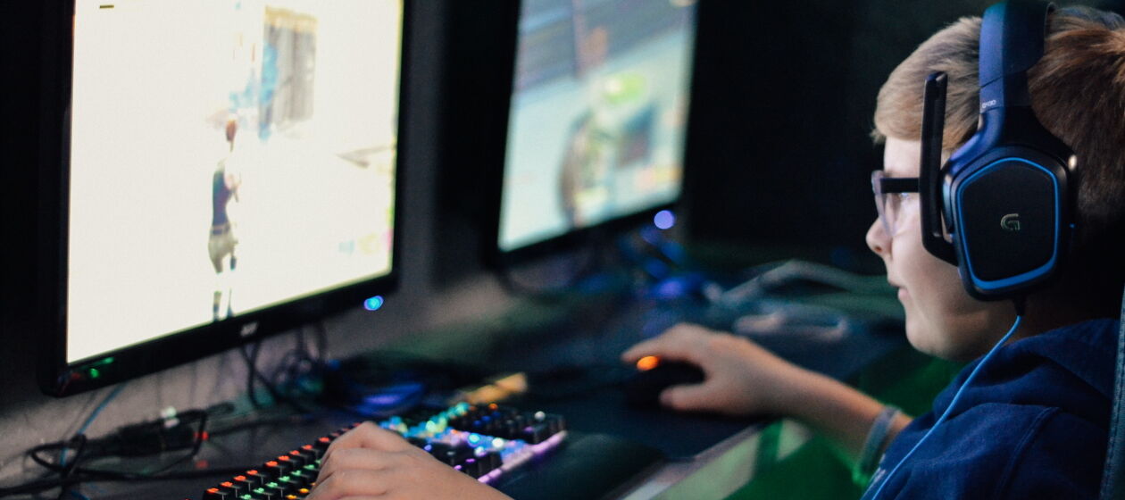 Ein Junge mit Headset sitzt vor zwei Bildschirmen und spielt ein Computerspiel